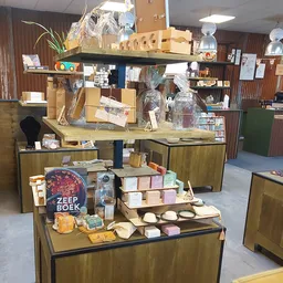 Uitgestalde tweedehands spullen op houten vitrines, waaronder boeken, kaarsen, servies en decoratieve artikelen