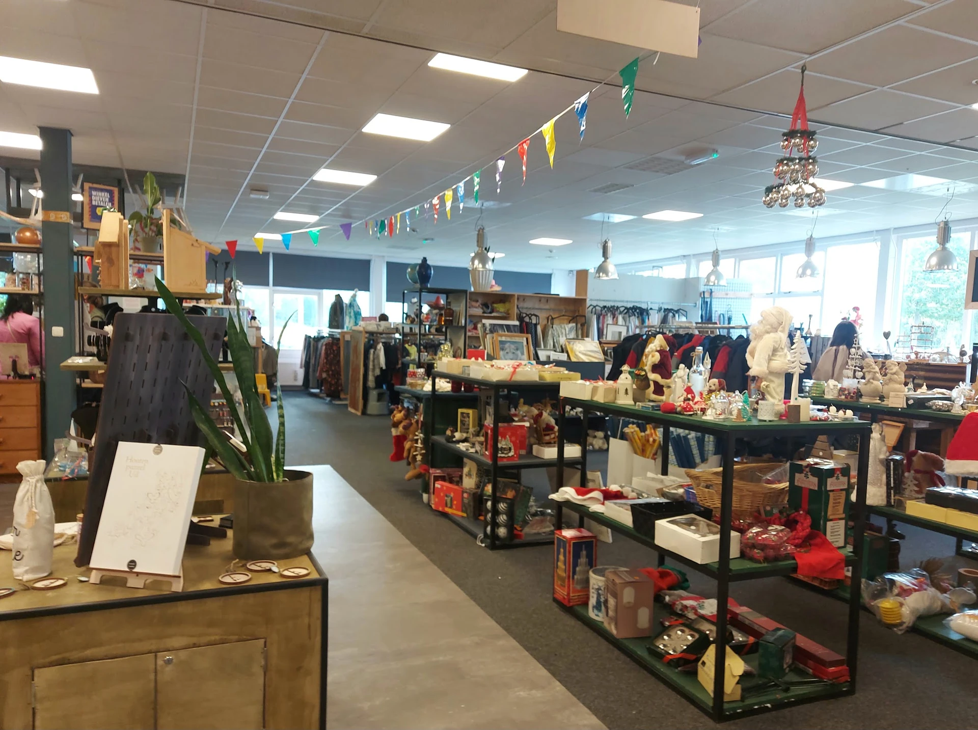 Winkelvloer met diverse meubels, decoratie en huishoudartikelen op tafels en stellingen, versierd met slingers