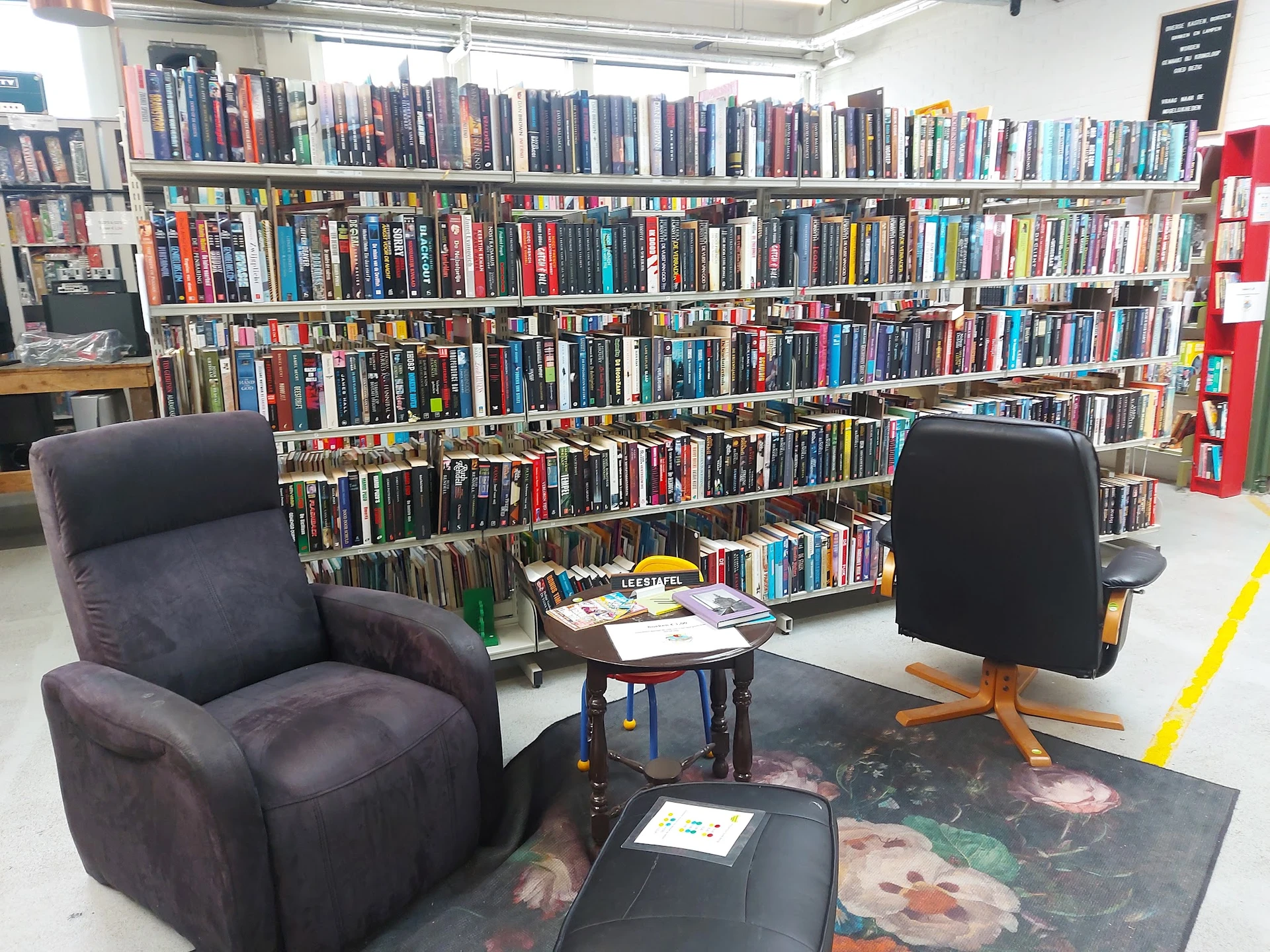 Zithoeken met twee fauteuils voor een grote boekenstelling vol dvd's en films in de kringloopwinkel