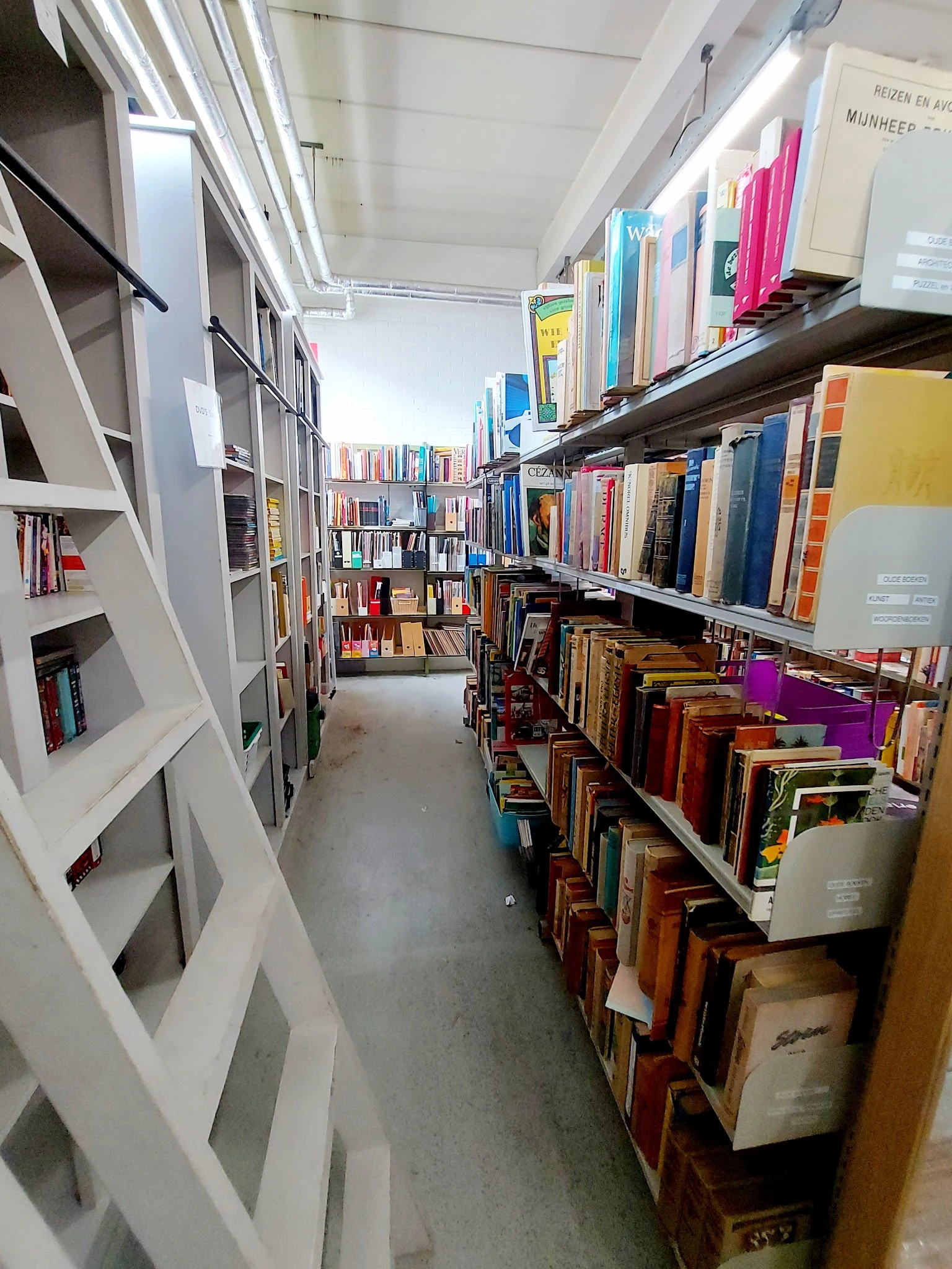 Gangpad tussen boekenrekken en kasten in kringloopwinkel met diverse boeken en spullen