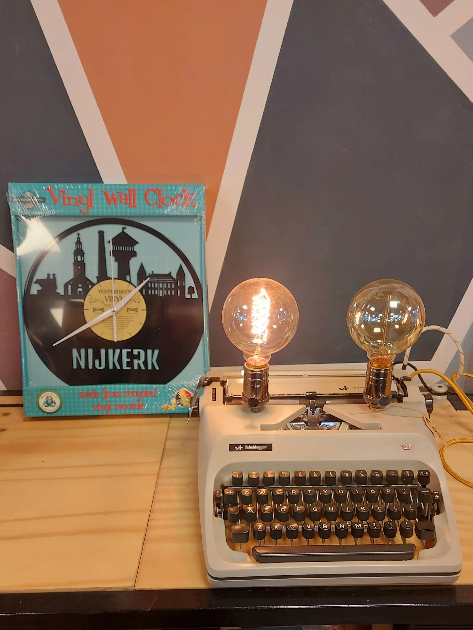 Twee vintage bureaulampen met gloeikolf op een typemachine, naast een vinylklok met Nijkerk skyline