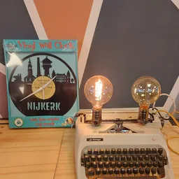 Twee vintage bureaulampen met gloeikolf op een typemachine, naast een vinylklok met Nijkerk skyline