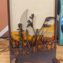 Decoratief kunstwerk van donkerpaars metaal met bloemen- en grassen-silhouetten tegen geel en oranje achtergrond