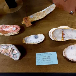 Uitgestalde handgemaakte items met decoratieve schilderingen op houten schelpvormen op een tafel