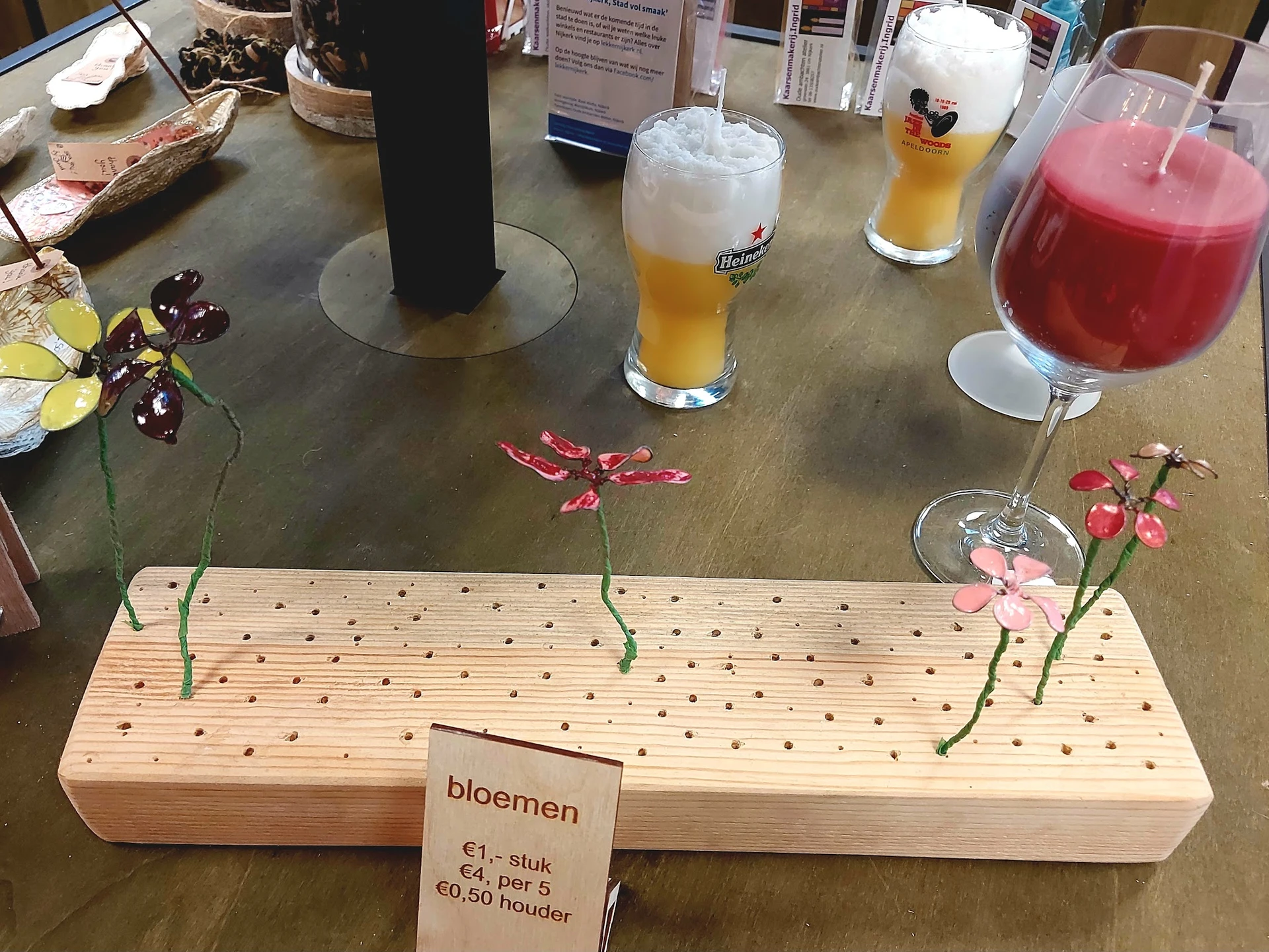 Houten bloemschikbord met bloemen en prijskaartje, omgeven door glazen met dranken op een grijze tafel