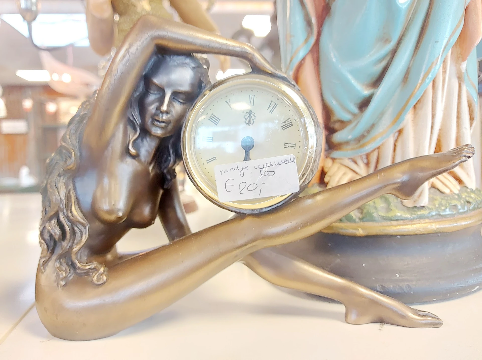 Bronzen decoratief klokje met vrouwenfiguur, wijzerplaat met Romeinse cijfers, prijskaartje zichtbaar