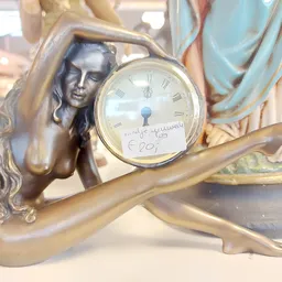 Bronzen decoratief klokje met vrouwenfiguur, wijzerplaat met Romeinse cijfers, prijskaartje zichtbaar