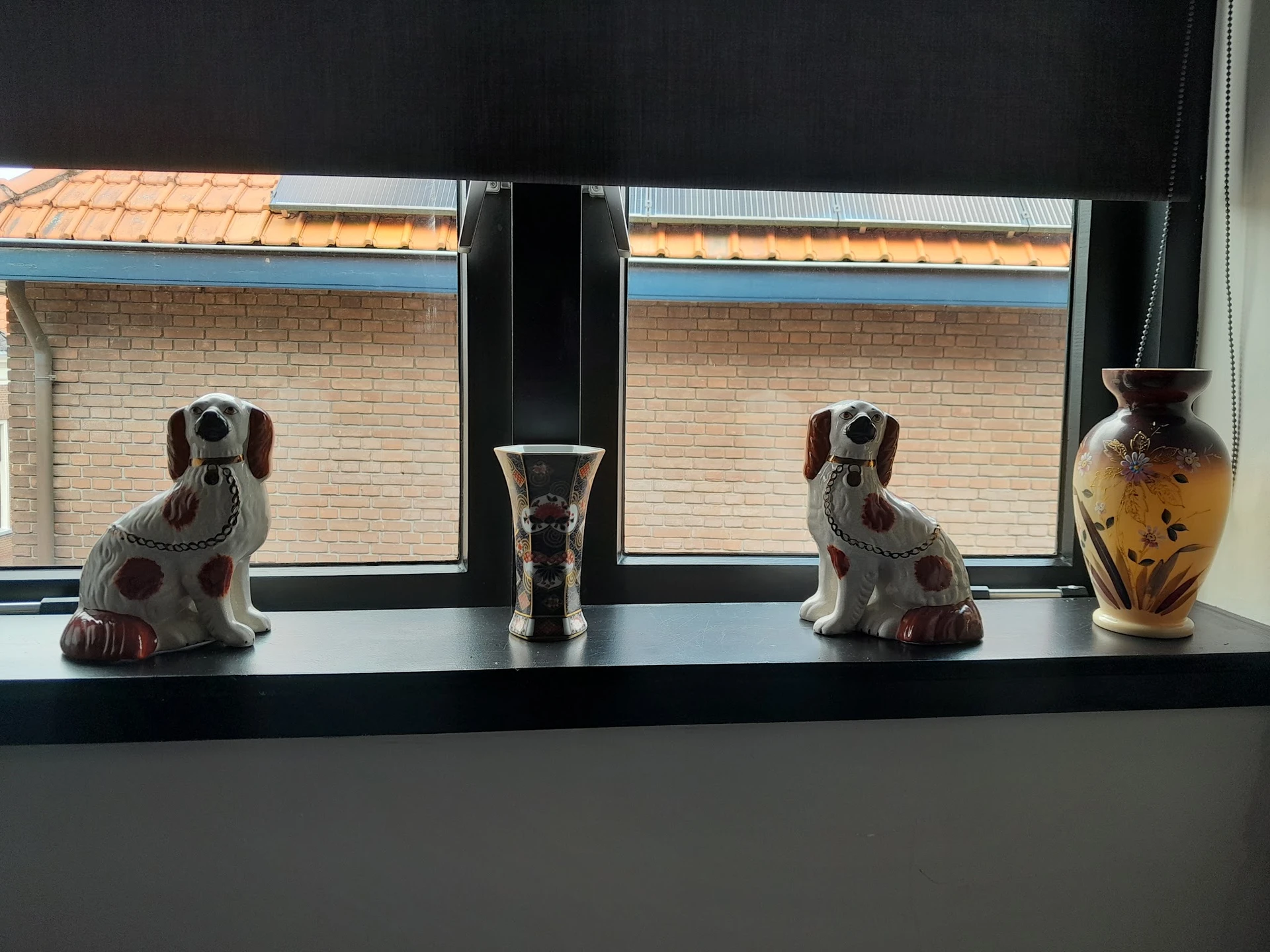 Twee porseleine hondenbeeldjes, een vaas en een decoratief object op een vensterbank