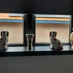 Twee porseleine hondenbeeldjes, een vaas en een decoratief object op een vensterbank