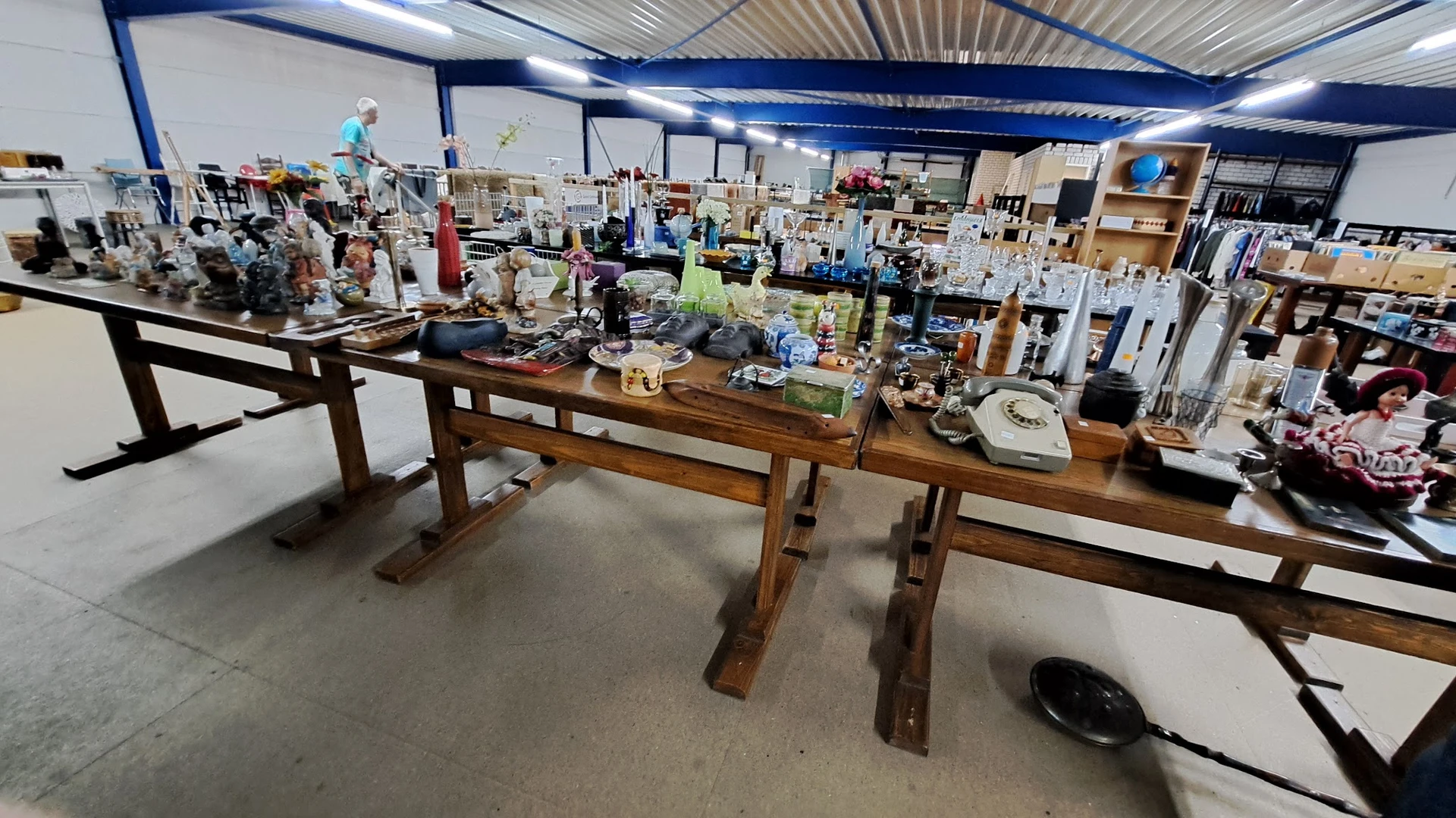 Winkelvloer met houten tafel en diverse huishoudelijke spullen en meubels uitgestald in een groot magazijnachtig pand