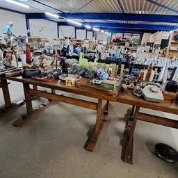 Winkelvloer met houten tafel en diverse huishoudelijke spullen en meubels uitgestald in een groot magazijnachtig pand