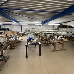 Ruim magazijnachtig interieur met houten werktafels, stellingen en assortiment huishoudelijke spullen en decoratieartikelen