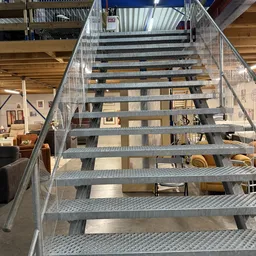Metalen trap met trapleuning in een kringloopwinkel, uitzicht op meubels en spullen op de begane grond