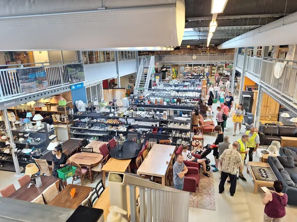 Overzicht van de winkelvloer met tafels, stellingen, meubels en bezoekers in de kringloopwinkel