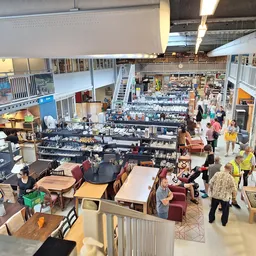 Overzicht van de winkelvloer met tafels, stellingen, meubels en bezoekers in de kringloopwinkel