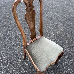Houten stoel met gesneden rugleuning en grijslinnen zitting, gezien van achteren.