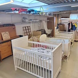 Winkelinterieur met babybedjes, speelgoed aan het plafond, kasten en kleding op hangers