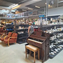 Winkelvloer met uitgestalde meubels, serviesgoed en een piano, met klanten die rondkijken