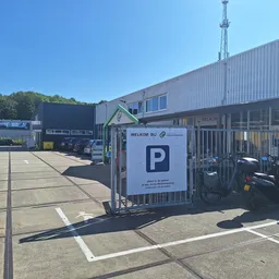 Parkeerplaats met welkomstbord en bedrijfsgebouw van kringloopwinkel