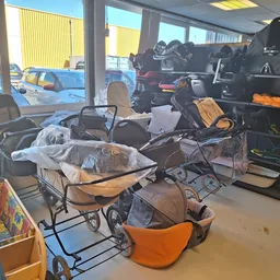 Verschillende tweedehands kinderwagens en buggy's in de winkel, gedeeltelijk verpakt en opgestapeld.