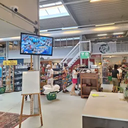 Winkelvloer met diverse meubelstukken, rekken met spullen en bezoekers in een ruime kringloopwinkel