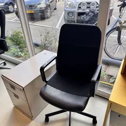 Zwarte bureaustoel met armleuningen en witte ladekast op winkelvloer