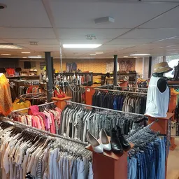 Overzicht van winkelinterieur met kledingrekken vol tweedehands kleding in verschillende kleuren en stijlen