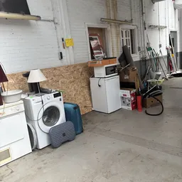 Garage of opslagruimte met witgoedartikelen, lamp, matras en verschillende huishoudelijke spullen