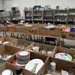 Dozen met serviesgoed, borden, kopjes en glazen uitgestald in de kringloopwinkel