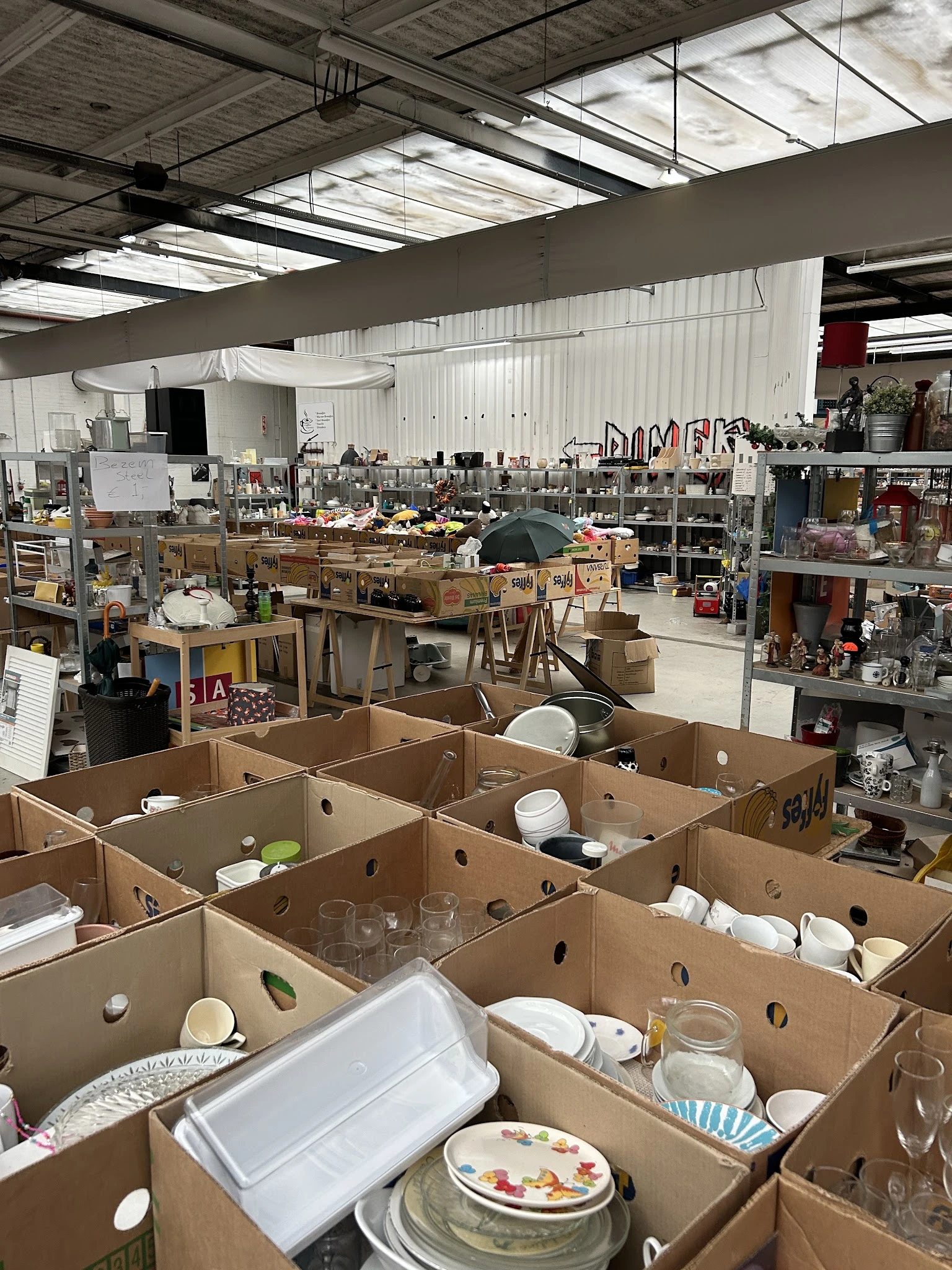 Overzicht van de kringloopwinkel met dozen op de voorgrond en rekken met spullen op de achtergrond