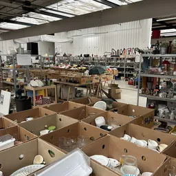 Overzicht van de kringloopwinkel met dozen op de voorgrond en rekken met spullen op de achtergrond