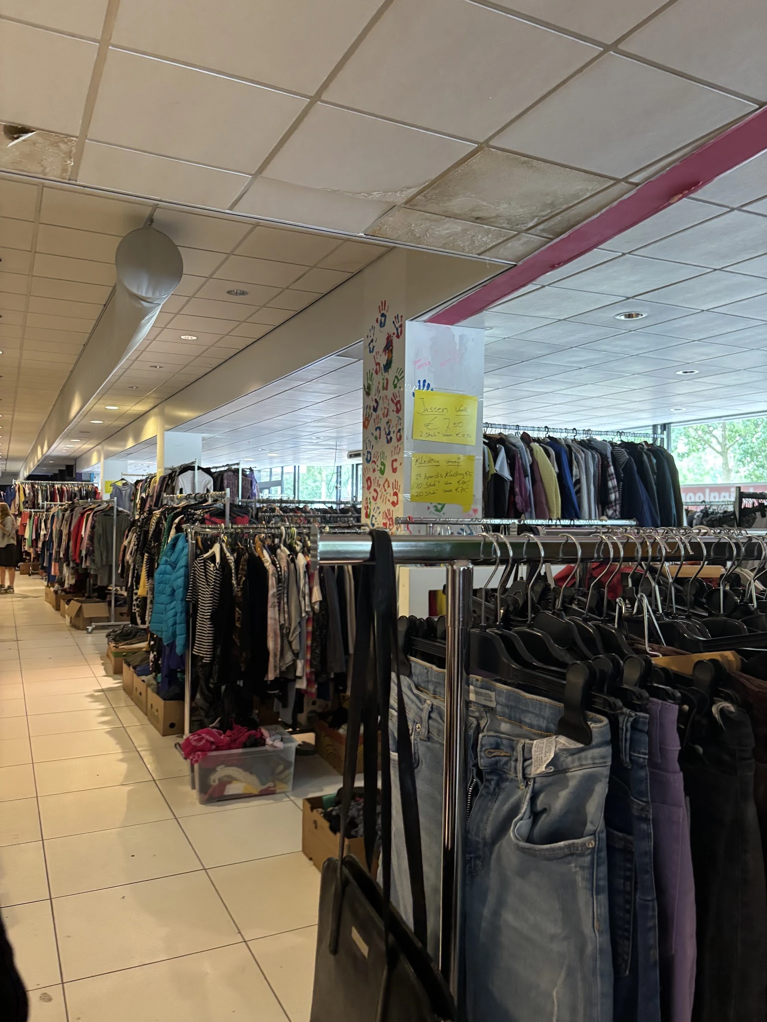 Rekken met tweedehands kleding, vooral jassen en broeken in donkere kleuren