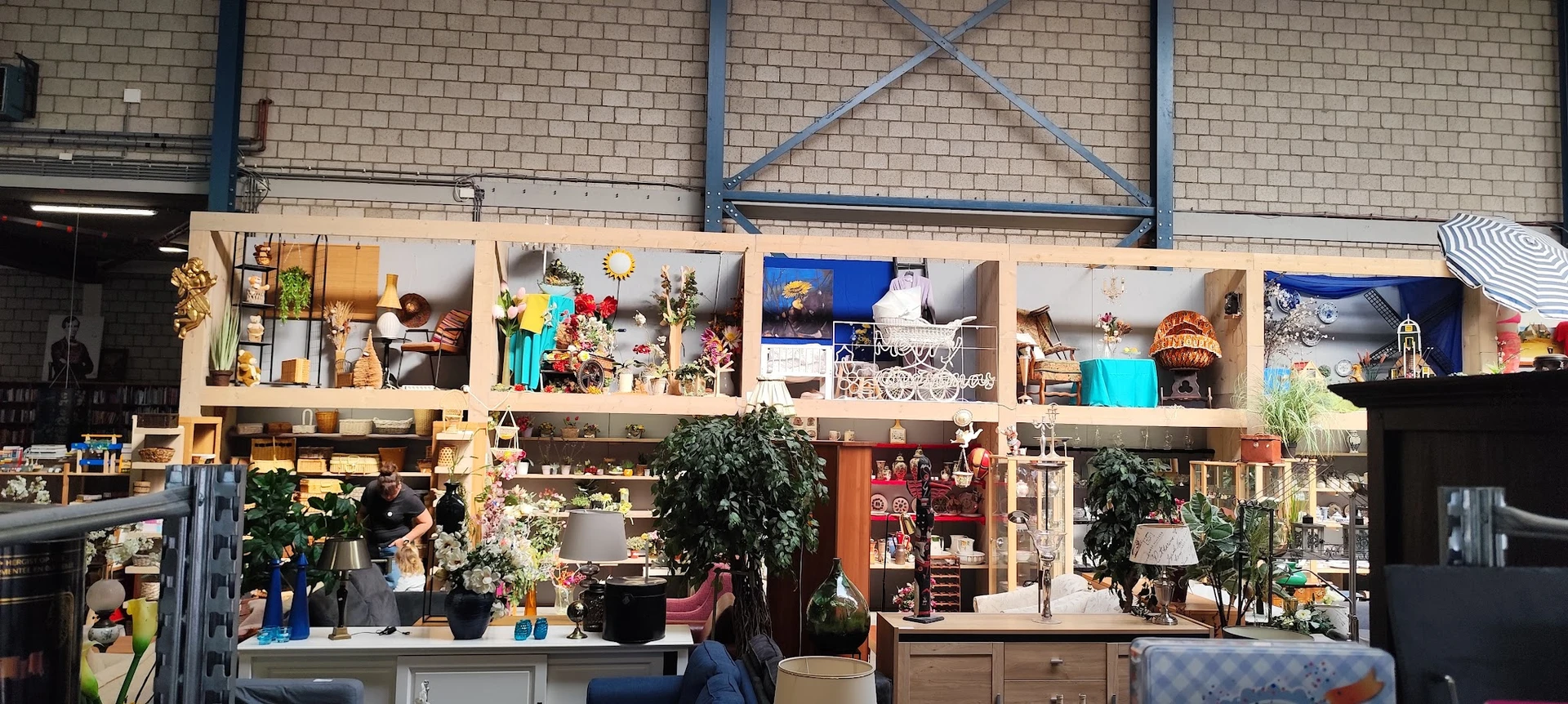 Interieur van kringloopwinkel met houten stellingen vol huishoudartikelen, decoraties, planten en meubels tegen bakstenen muu