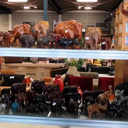 Stellingen met houten beelden van olifanten en andere decoratieve dierenfiguren in verschillende maten en kleuren
