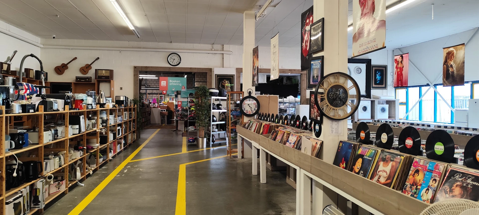 Winkelvloer met gele richtingslijnen, stellingen met boeken, vinyl records, klokken en decoratie aan de muur
