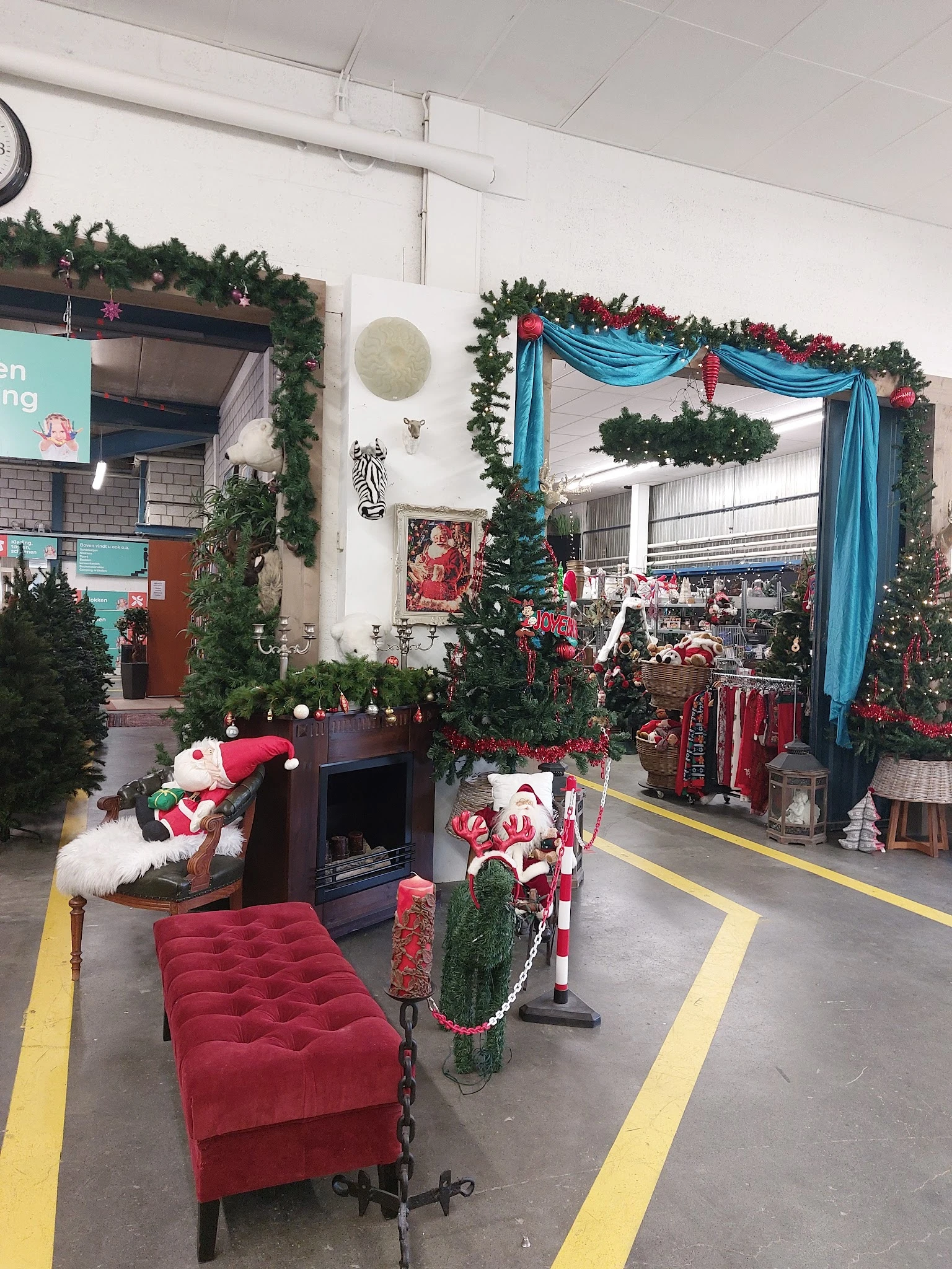 Kersversierde winkelruimte met groene guirlandes, rode decoraties, blauwe linten en kerstmanfiguren bij de ingang