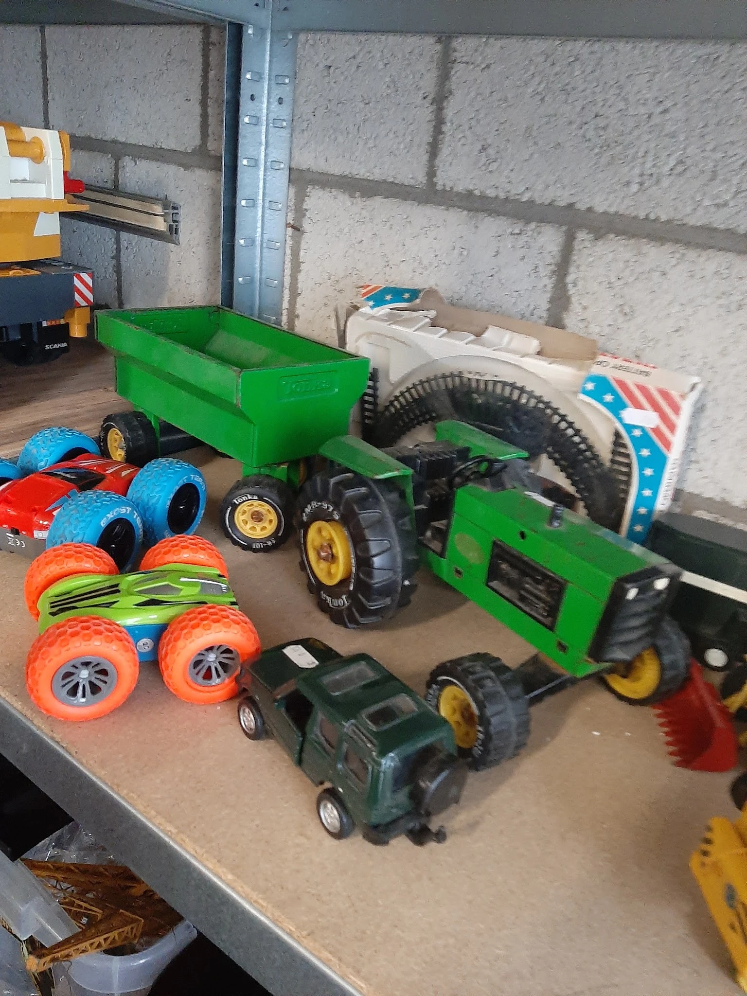 Verzameling tweedehands speelgoed waaronder groene trailers, rode en blauwe speelgoedauto's, oranje wielen en groene tractore