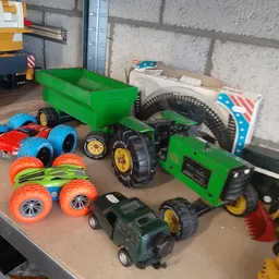 Verzameling tweedehands speelgoed waaronder groene trailers, rode en blauwe speelgoedauto's, oranje wielen en groene tractore