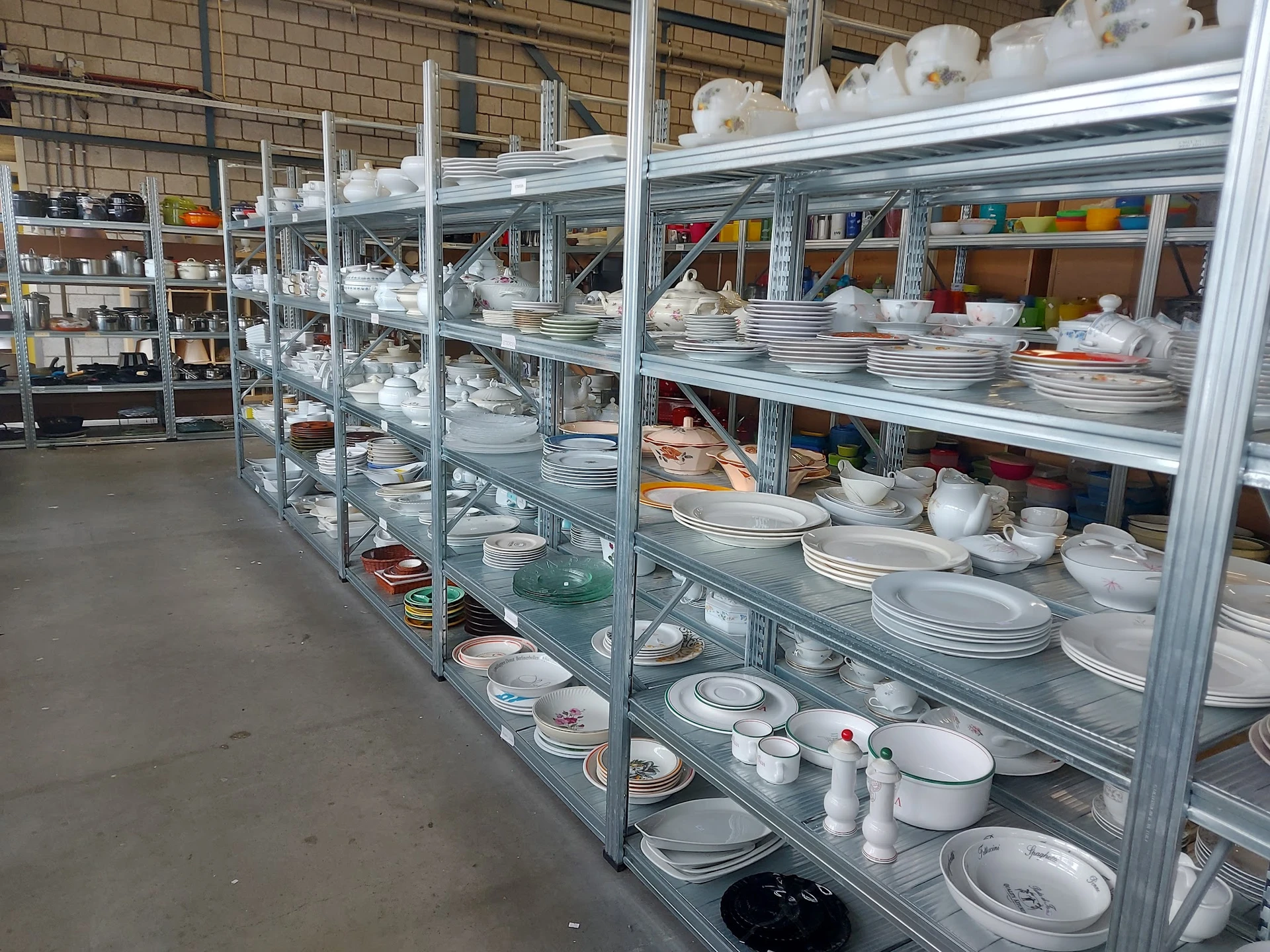 Stellingen vol serviesgoed, borden, schalen en ander huishoudelijk aardewerk uitgestald in een kringloopwinkel