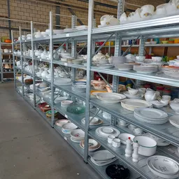 Stellingen vol serviesgoed, borden, schalen en ander huishoudelijk aardewerk uitgestald in een kringloopwinkel