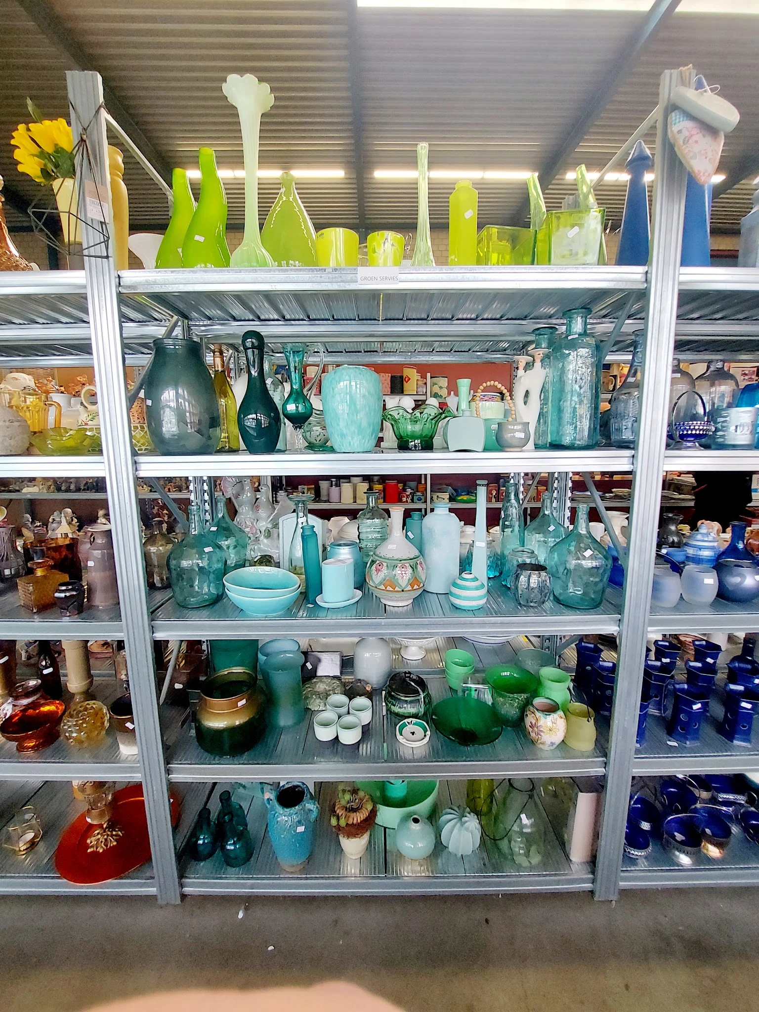 Metalen stellingkast met turquoise en groene huishoudelijke artikelen, vazen, kannen en serviesgoed netjes uitgestald