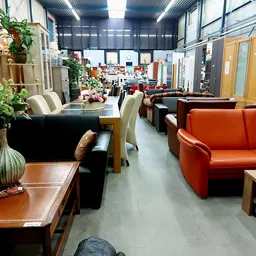 Winkelvloer met diverse meubels: zwarte tafel met stoelen, oranje bank, houten tafels en plantendecoratie
