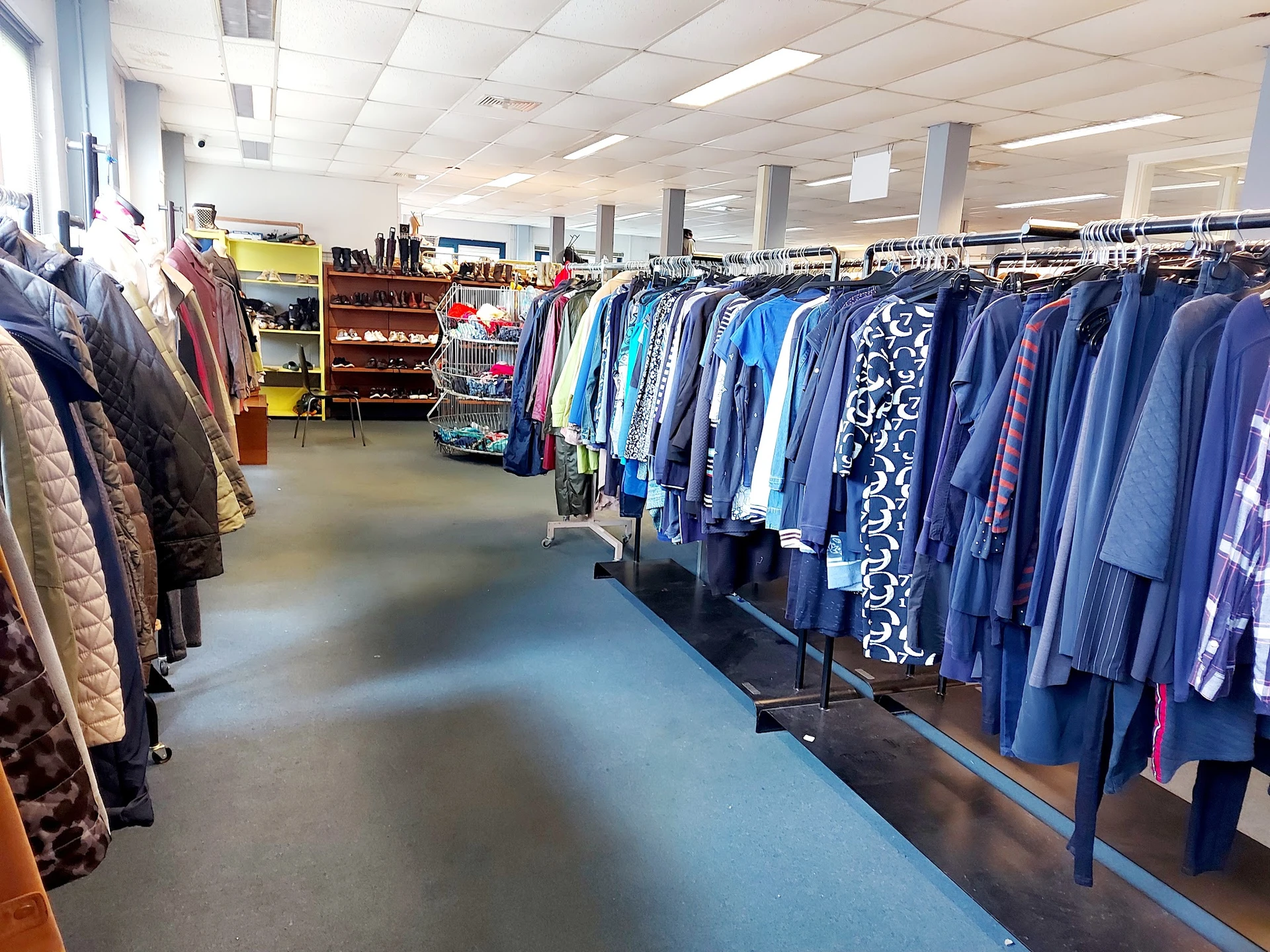 Rekken met tweedehands kleding, vooral jassen en jasjes in blauwe en paarse tinten