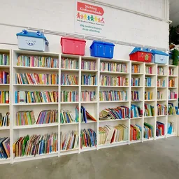 Witte boekenkasten vol met tweedehands boeken in verschillende kleuren, met gekleurde opbergboxen bovenop