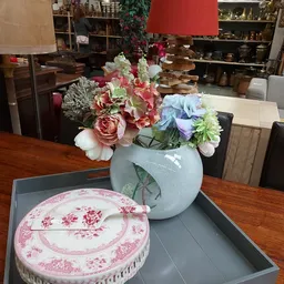 Blauwe vaas met roze en witte bloemen op houten tafel naast roze bord