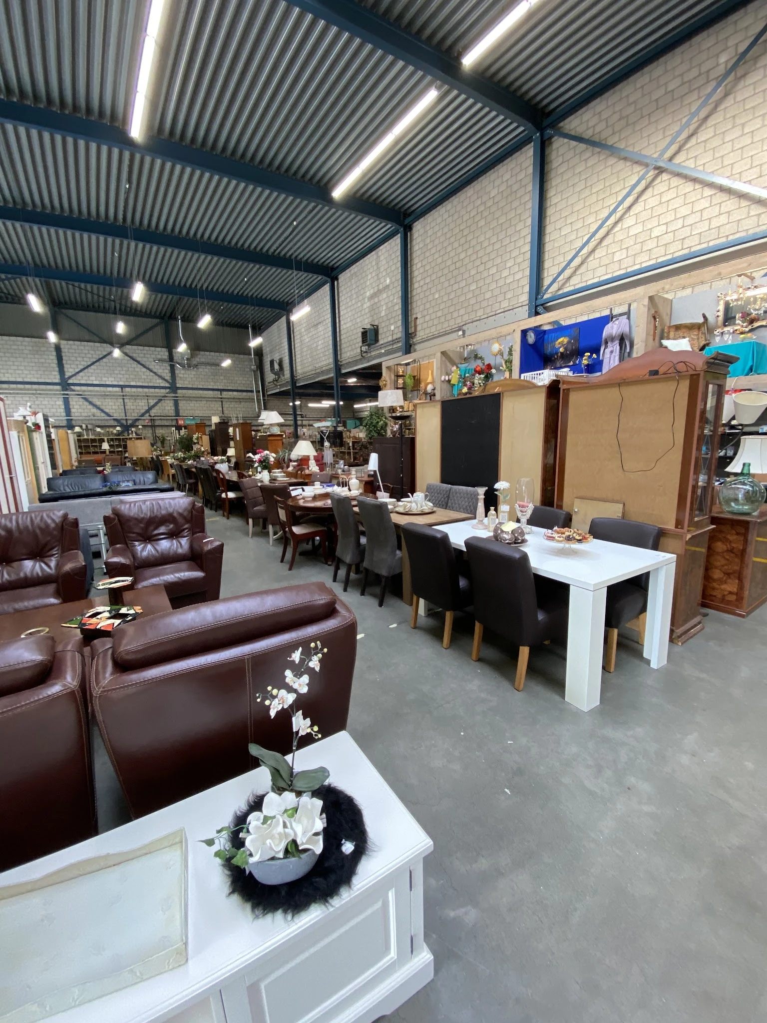Winkelvloer met meubels: bruine leren fauteuils vooraan, witte eettafel met zwarte stoelen, kasten en diverse meubels in het 