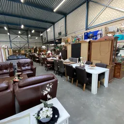 Winkelvloer met meubels: bruine leren fauteuils vooraan, witte eettafel met zwarte stoelen, kasten en diverse meubels in het 