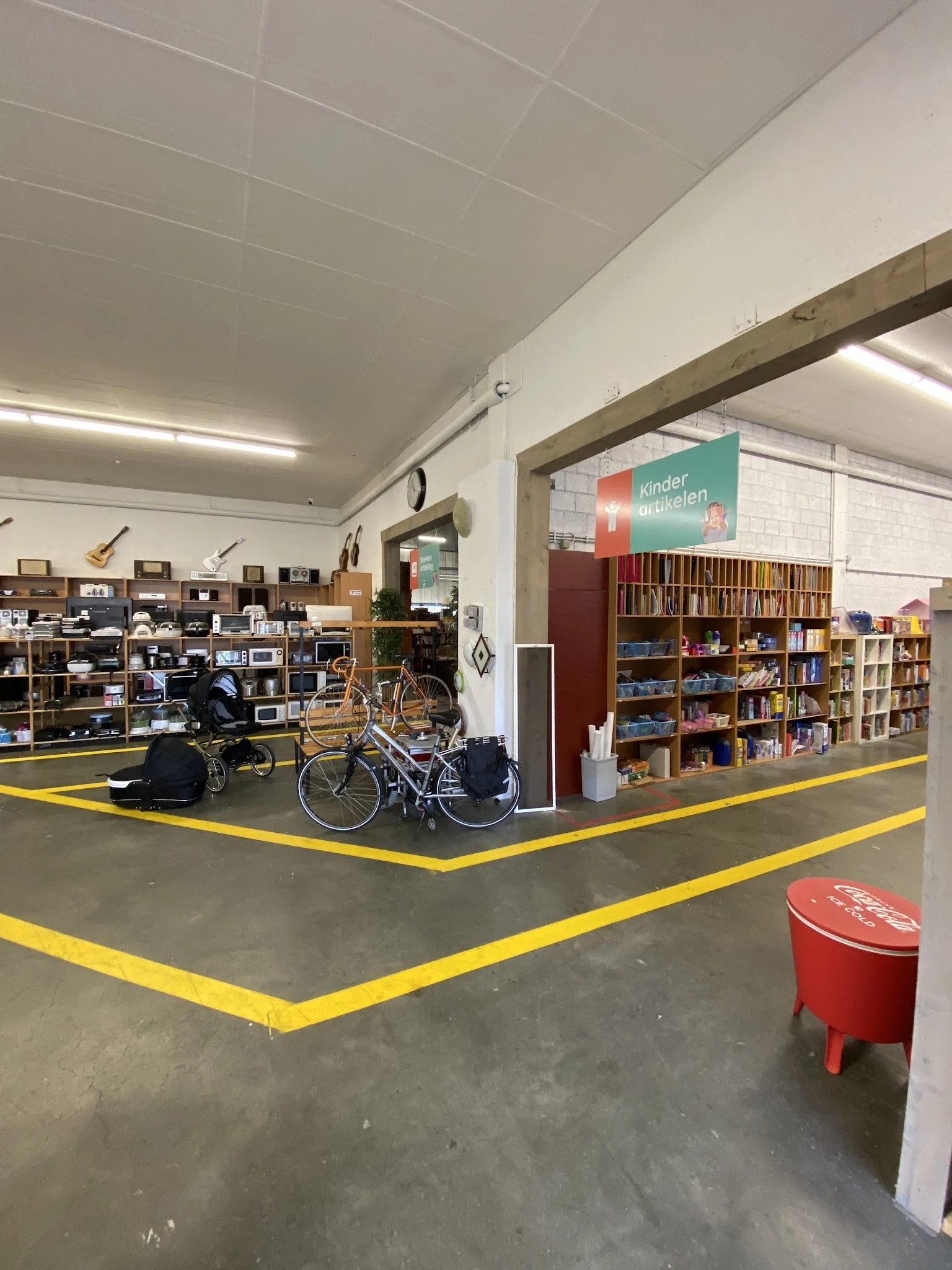 Winkelvloer met gele markeringslijnen, fietsen, boekenrekken en diverse spullen in een grote kringloopwinkel