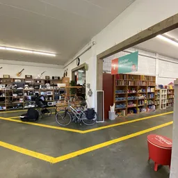 Winkelvloer met gele markeringslijnen, fietsen, boekenrekken en diverse spullen in een grote kringloopwinkel