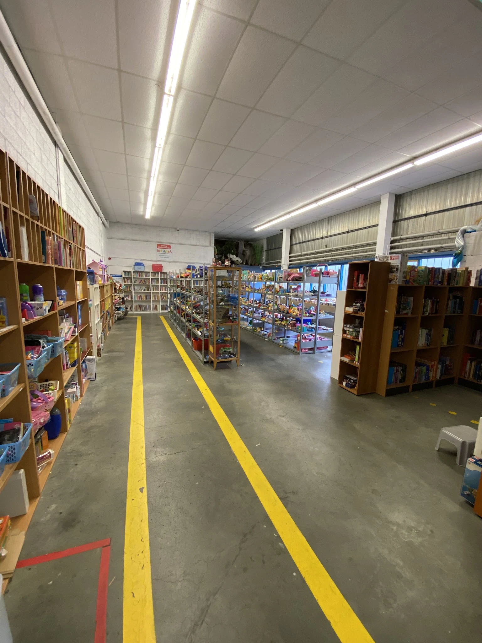 Winkelvloer met gele voetrijnmarkeringen, boekenkasten links, display met collectibles in het midden, houten stellingen recht